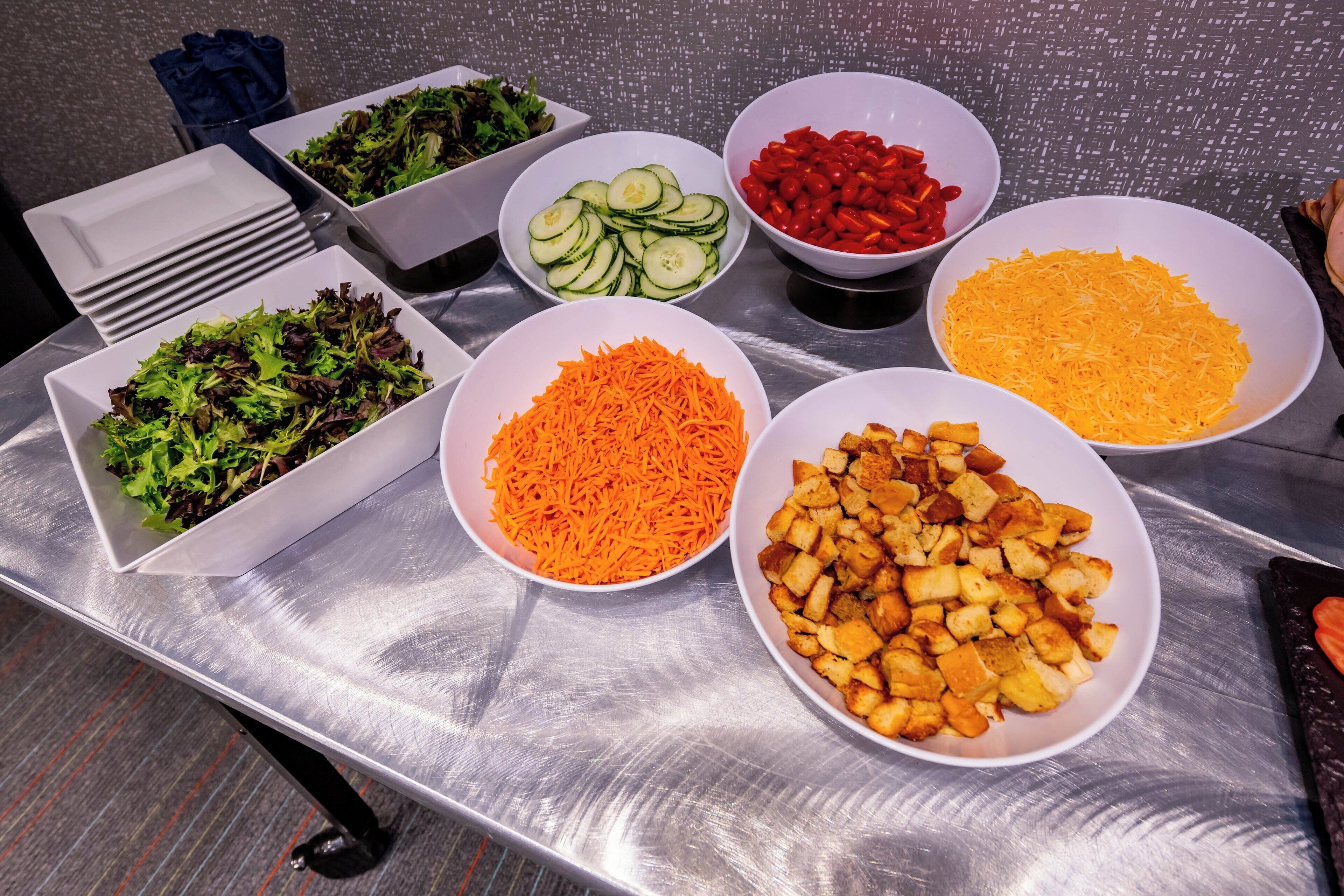 A buffet table with various food items including salads, shredded cheese, and cubed vegetables.