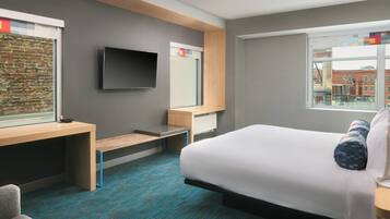 A hotel room with a bed, a desk, a television, and a window with a city view.