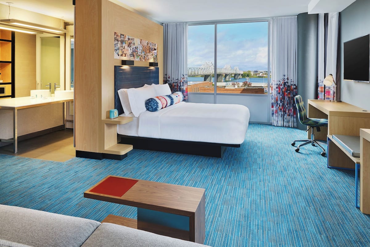A hotel room with a large bed, a desk, a chair, a TV, and a view of a bridge and water.