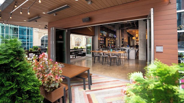 An indoor dining area with wooden tables and chairs, a bar area, and a view of the street outside.