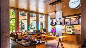 A modern coffee shop interior with a central island, wooden counter, and large windows.