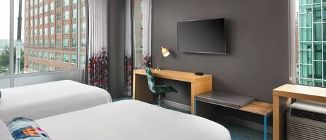 A hotel room with two beds, a desk, a chair, a TV, and a window with a city view.