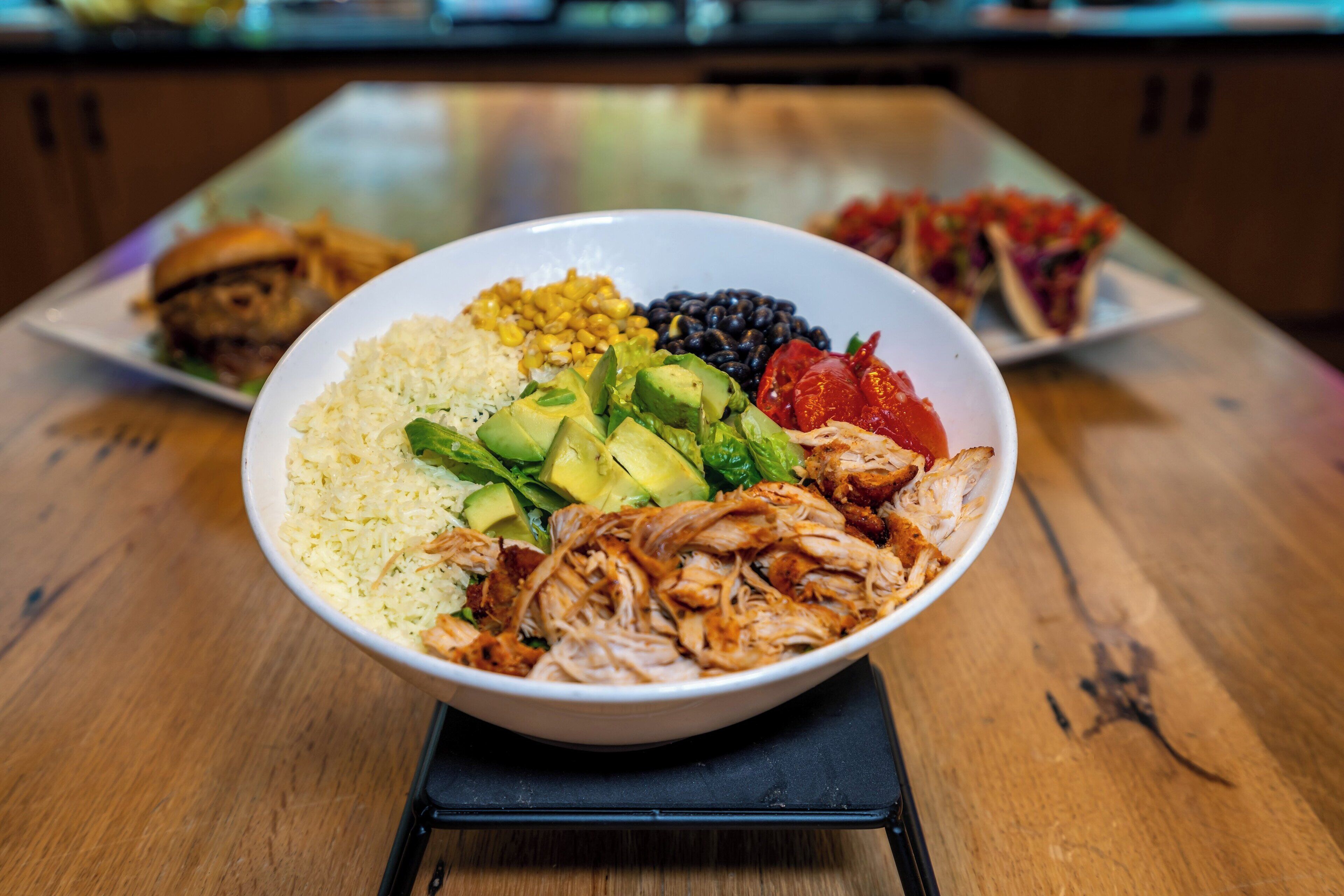 A bowl of food with rice, avocado, beans, and tomatoes on a wooden table.