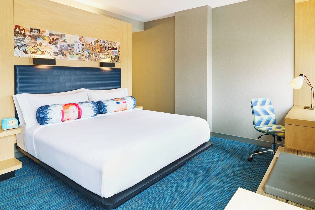 A hotel room with a large bed, a desk, a chair, and a wall with a collage of pictures.