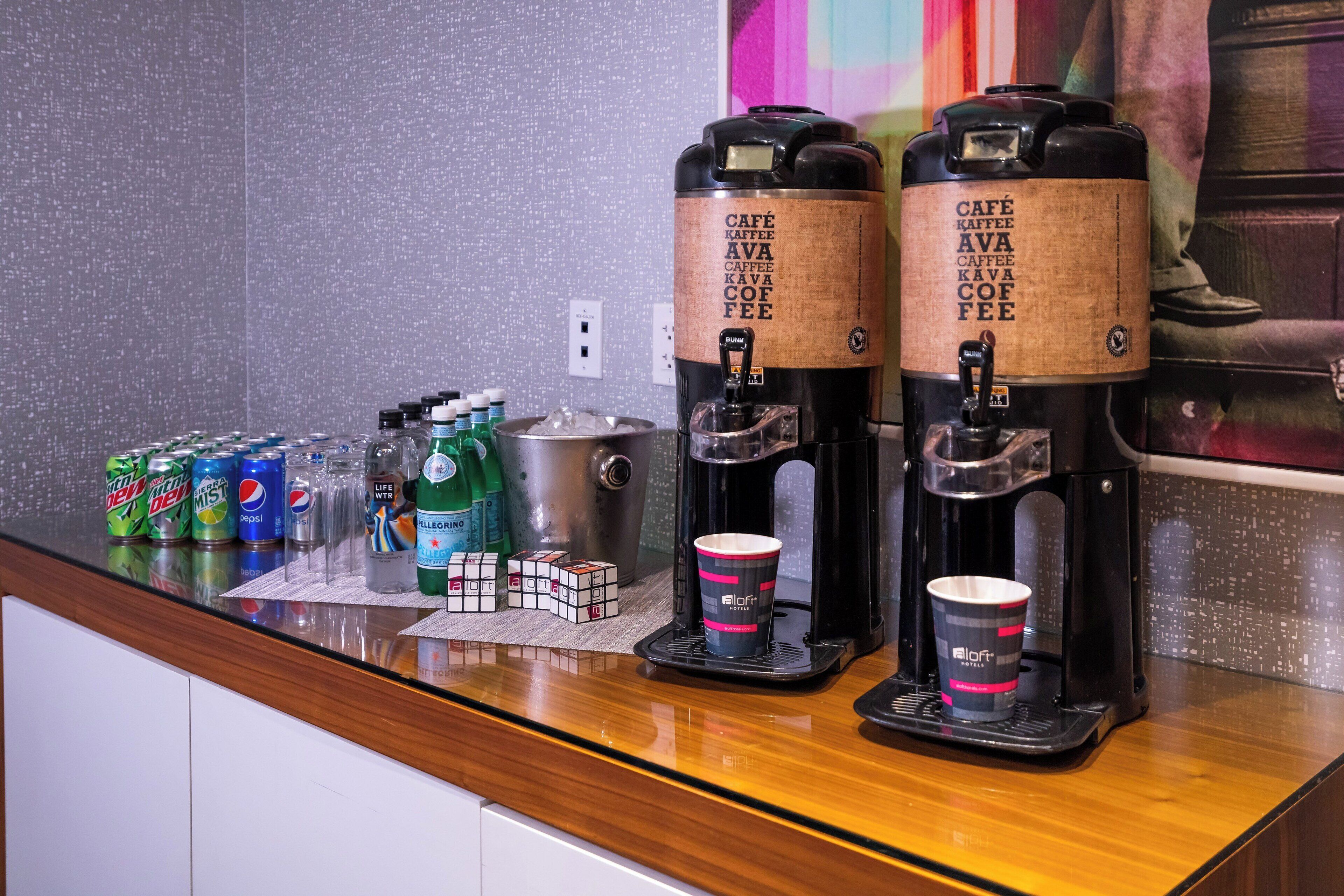 A coffee station with two coffee makers, a variety of beverages, and a Rubik's cube on the counter.