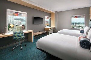 Habitación de hotel con cama, escritorio, silla, televisor y ventana con vista a la ciudad.