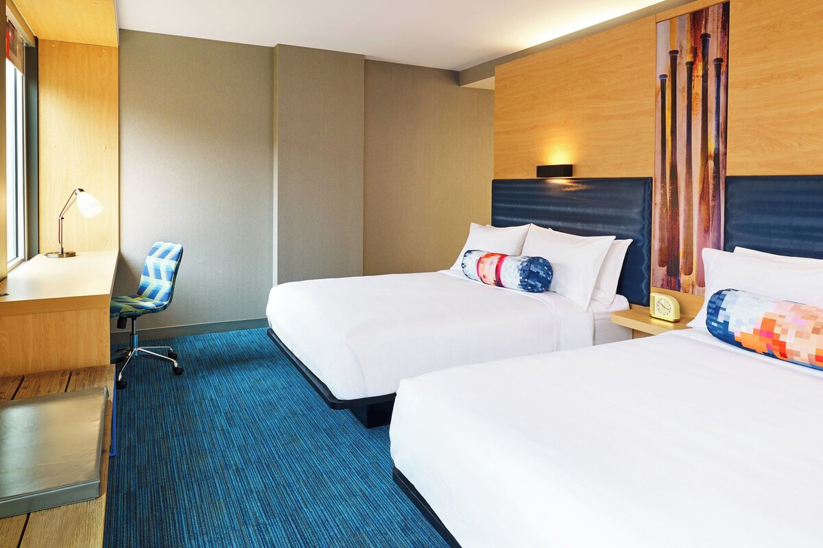 A hotel room with two beds, a desk, a chair, and a carpeted floor.