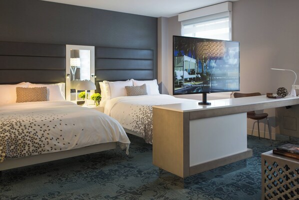 A hotel room with two beds, a TV, a desk, and a chair.