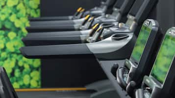 A row of treadmills with digital screens, set against a green leafy wall.