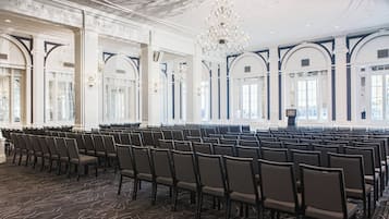 Un salón amplio y elegantemente decorado con filas de sillas, un atril y ventanas grandes.