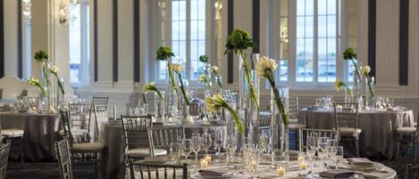 Comedor formal con mesas redondas dispuestas para una comida, con copas, platos y velas.