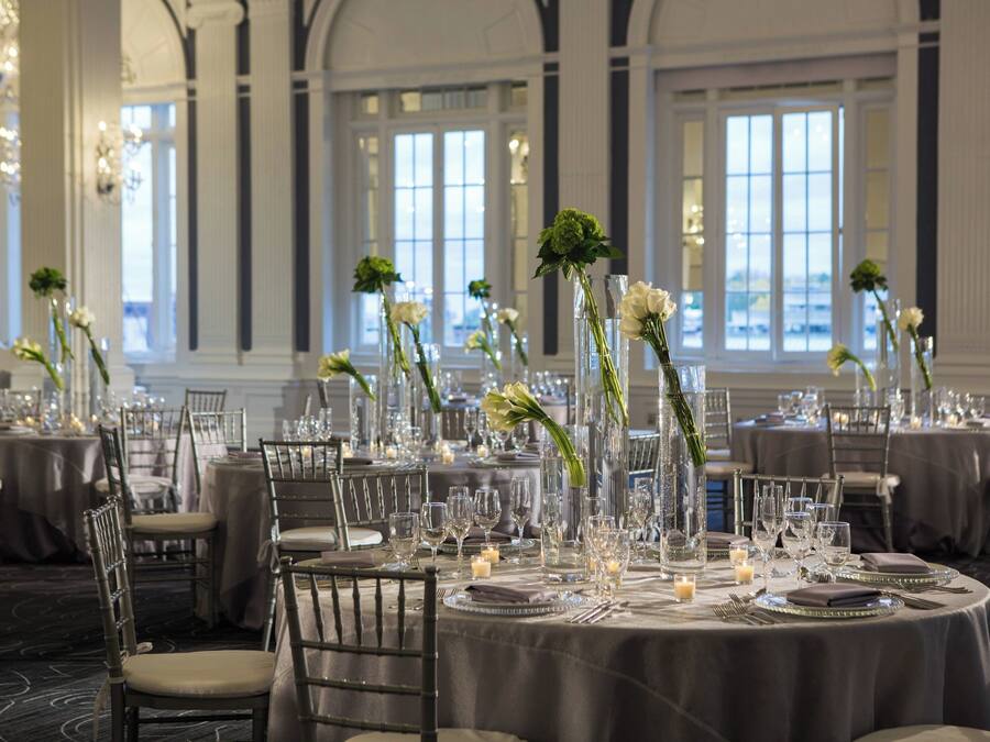 Une salle à manger élégante, avec des tables rondes dressées pour un repas, où l’on peut admirer de beaux verres, de l’argenterie et des bougies.