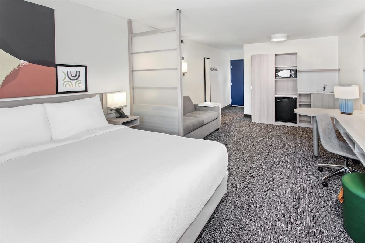 A hotel room with a large bed, a desk, a chair, and a kitchenette.