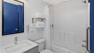 Un baño moderno con lavamanos, inodoro y bañera blancos. Hay una cortina de ducha y un pasamanos a la derecha.