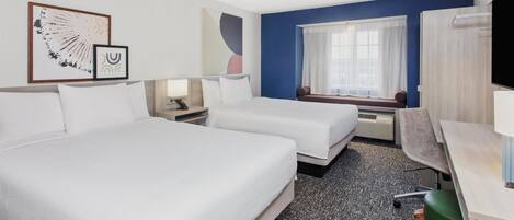 Ett hotellrum med två sängar, ett skrivbord, en stol, en TV och ett fönster med gardiner.