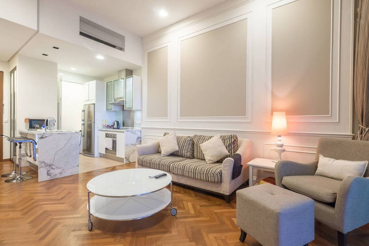 A modern living room with a sofa, armchairs, a coffee table, and a kitchen in the background.