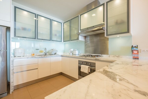 A modern kitchen with white cabinets, a stainless steel range hood, and a marble countertop.