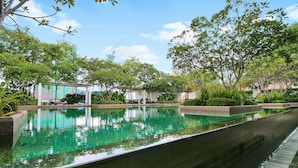 A swimming pool with clear water, surrounded by greenery and a building in the background. - Home Suites by Marina (George Town)