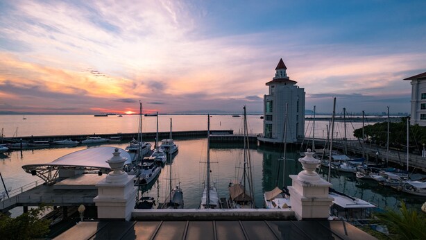 A marina with boats docked, a prominent white tower, and a sunset in the background. - Home Suites by Marina (George Town)