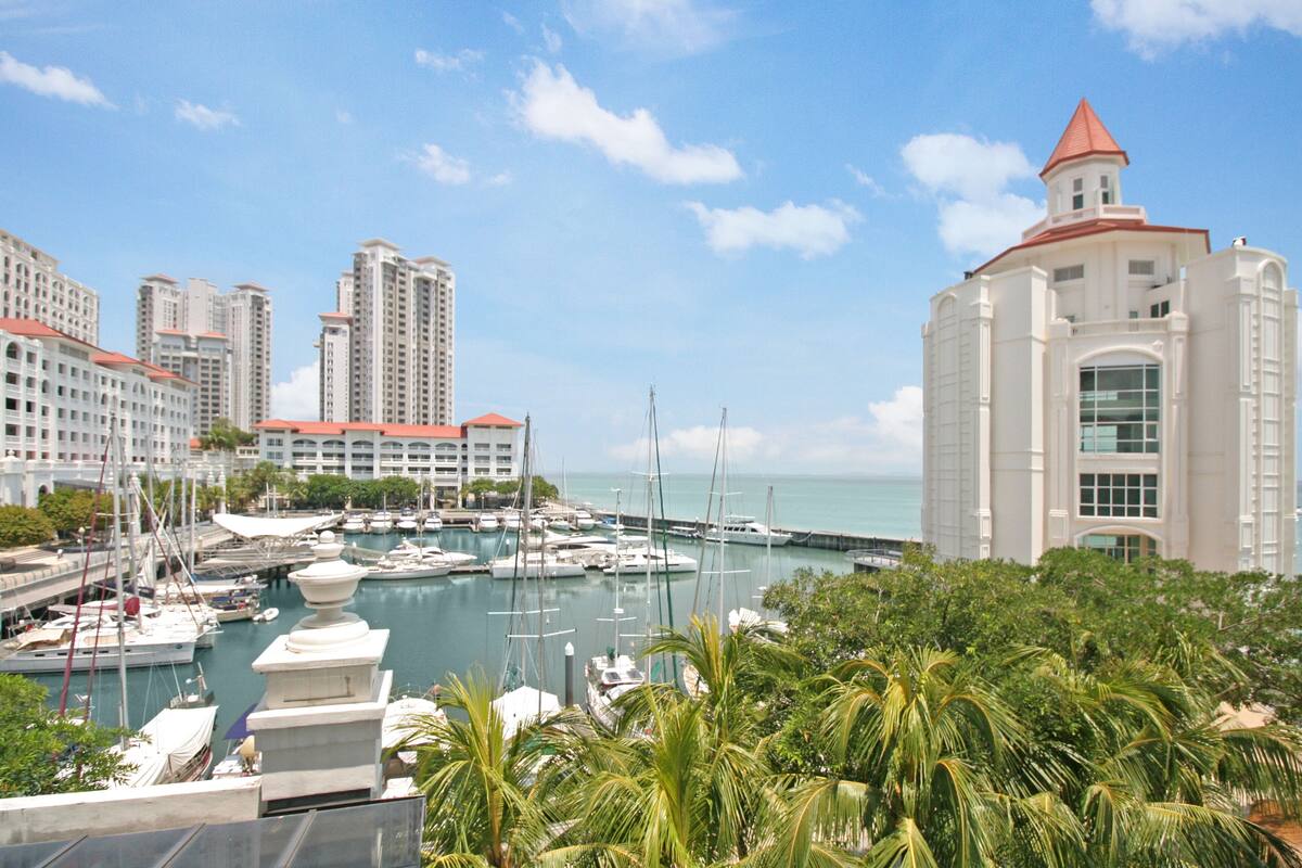 A marina with multiple boats docked, surrounded by high-rise buildings and lush greenery.
