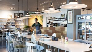 A modern cafe with multiple tables and chairs, a counter with a menu, and a display case with items. - Home Suites by Marina (George Town)