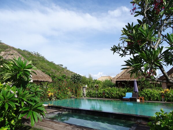 A pool area with thatched-roof structures, lounge chairs, and lush greenery.
