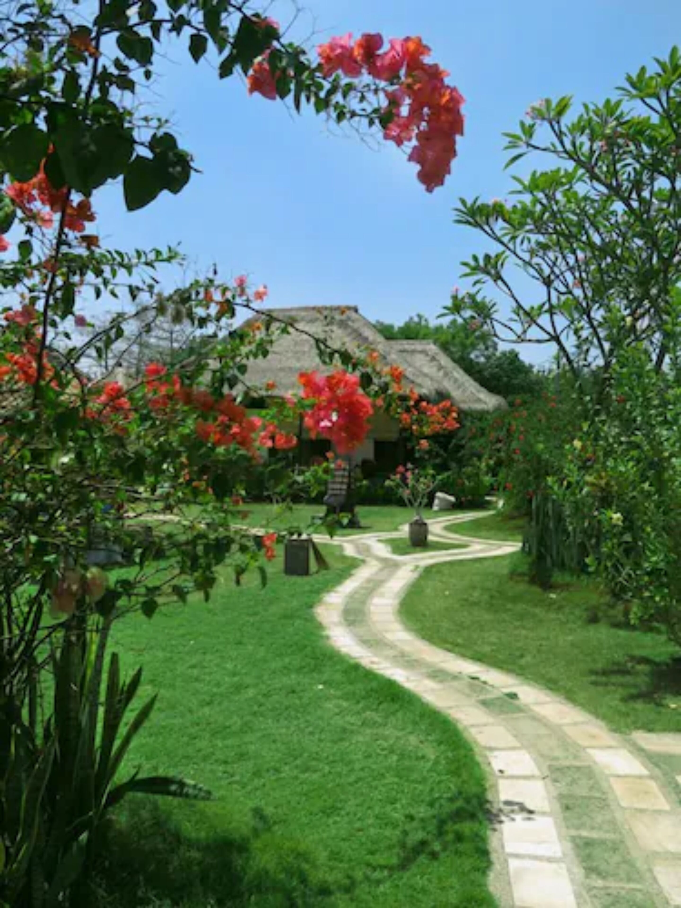 Un sendero en un jardín que lleva a una casa con techo de paja.