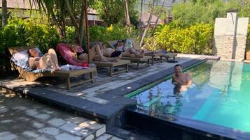 Un espace aménagé au bord de la piscine, avec des chaises longues et une personne dans l’eau.