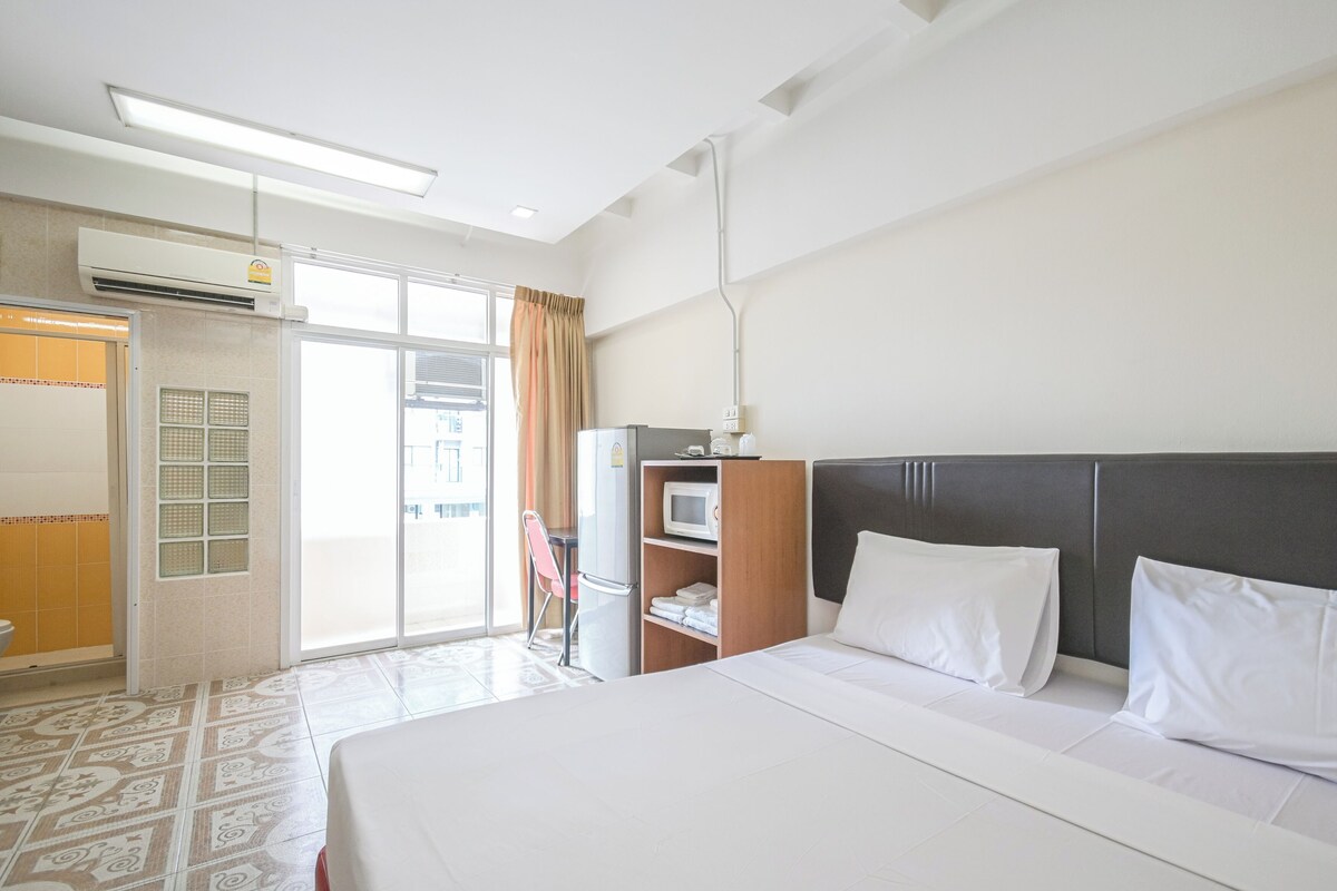 A hotel room with a bed, a desk, a microwave, and a sliding door to the outside.