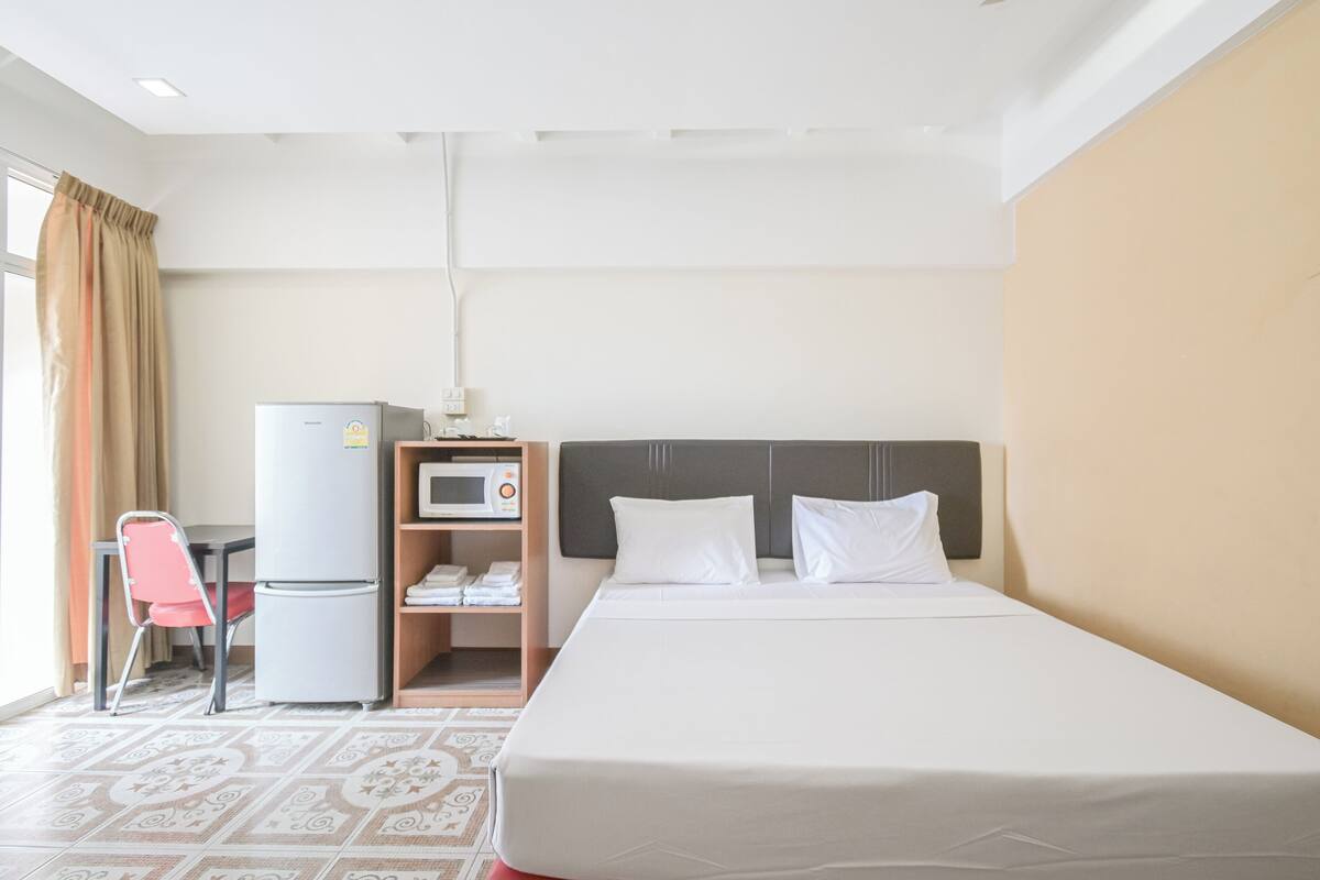 A hotel room with a bed, a desk with a refrigerator, a microwave, and a chair.