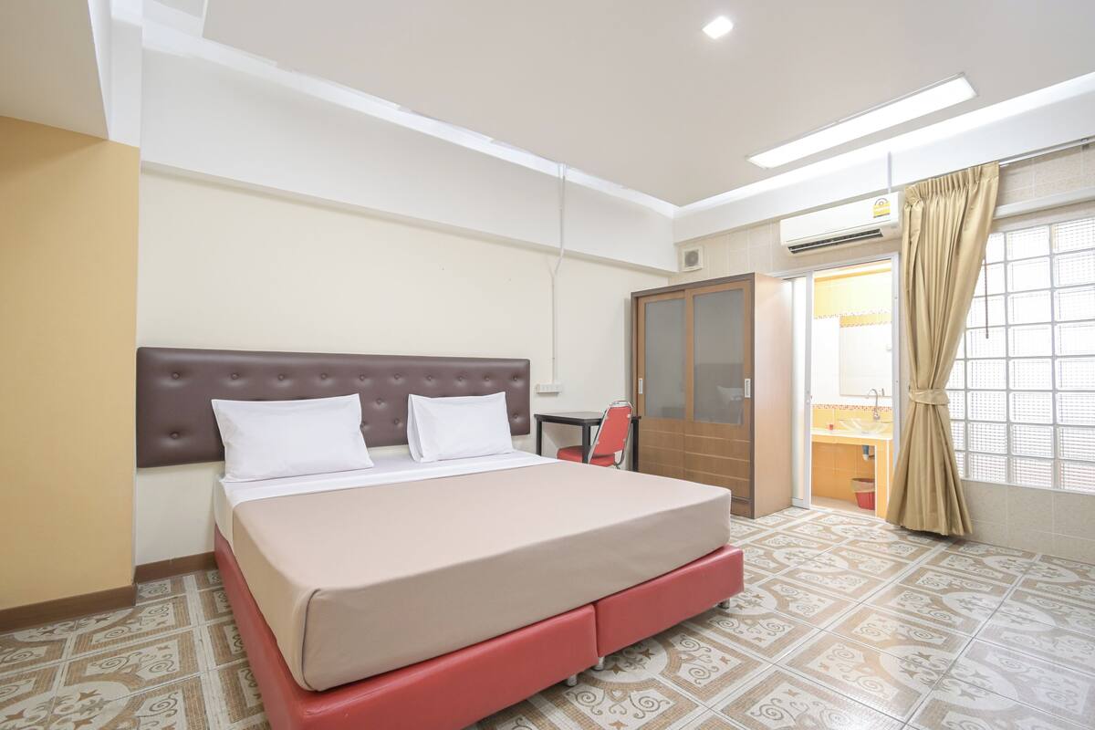 A hotel room with a bed, a wardrobe, a small table, and a window with curtains.