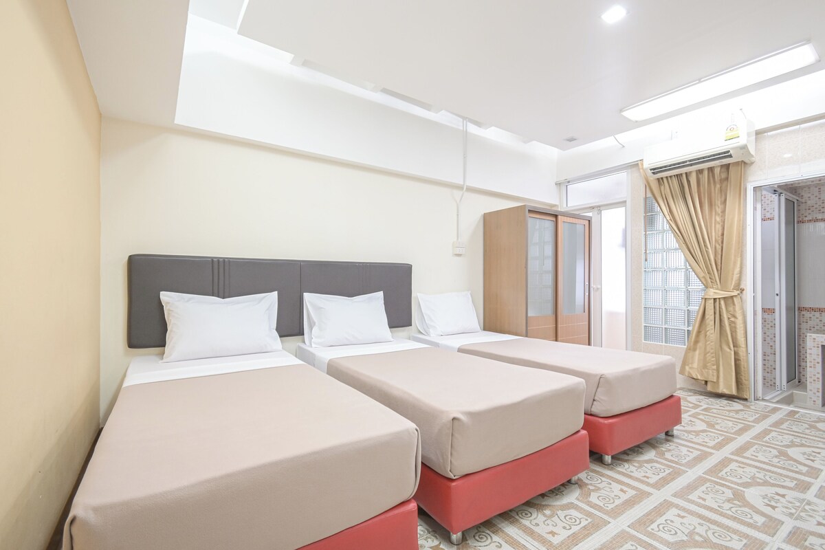 A hotel room with three single beds, a wardrobe, and a bathroom with a shower.