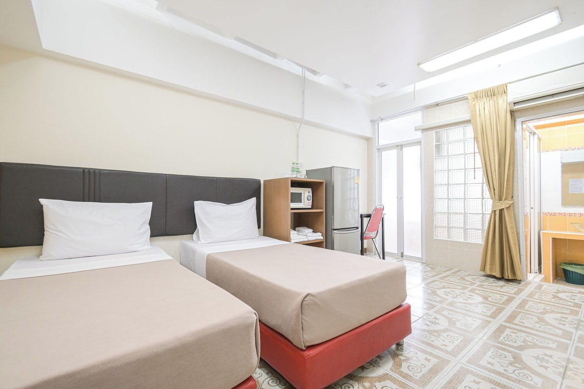 A hotel room with two beds, a microwave, a small table, and a window with curtains.