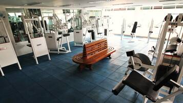 Een sportschool met diverse fitnessapparaten, een houten bank en een spiegelwand.