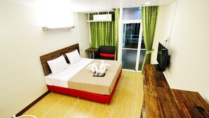 Ein Hotelzimmer mit Bett, Schreibtisch, Stuhl, Fernseher und einem Fenster mit Vorhängen.