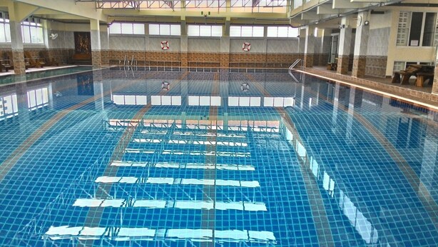 Ein Hallenbad mit klarem Wasser, gefliesten Wänden und Rettungsringen an der Wand.