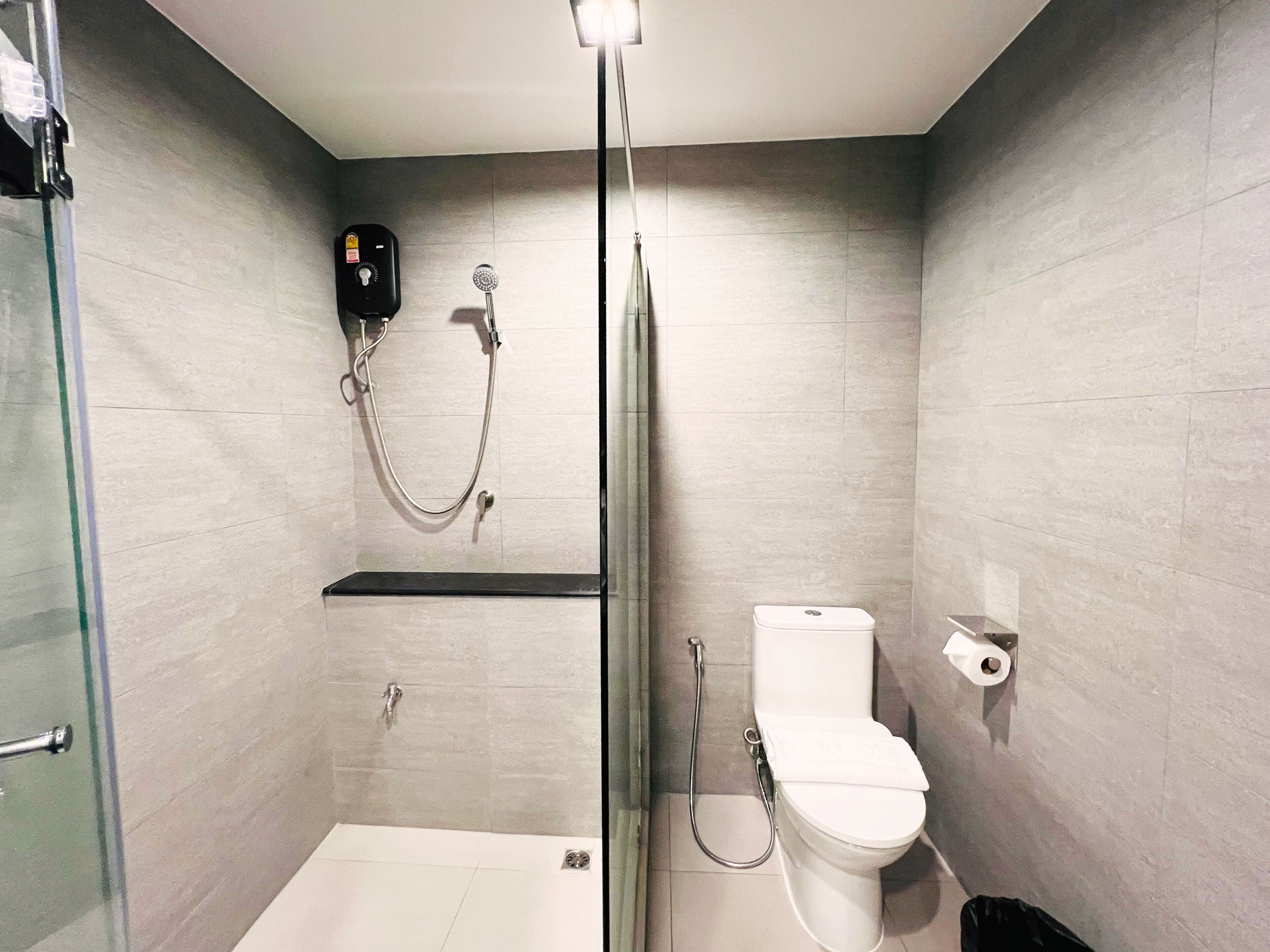 A modern bathroom with a glass-enclosed shower, a toilet, and a soap dispenser on the wall.