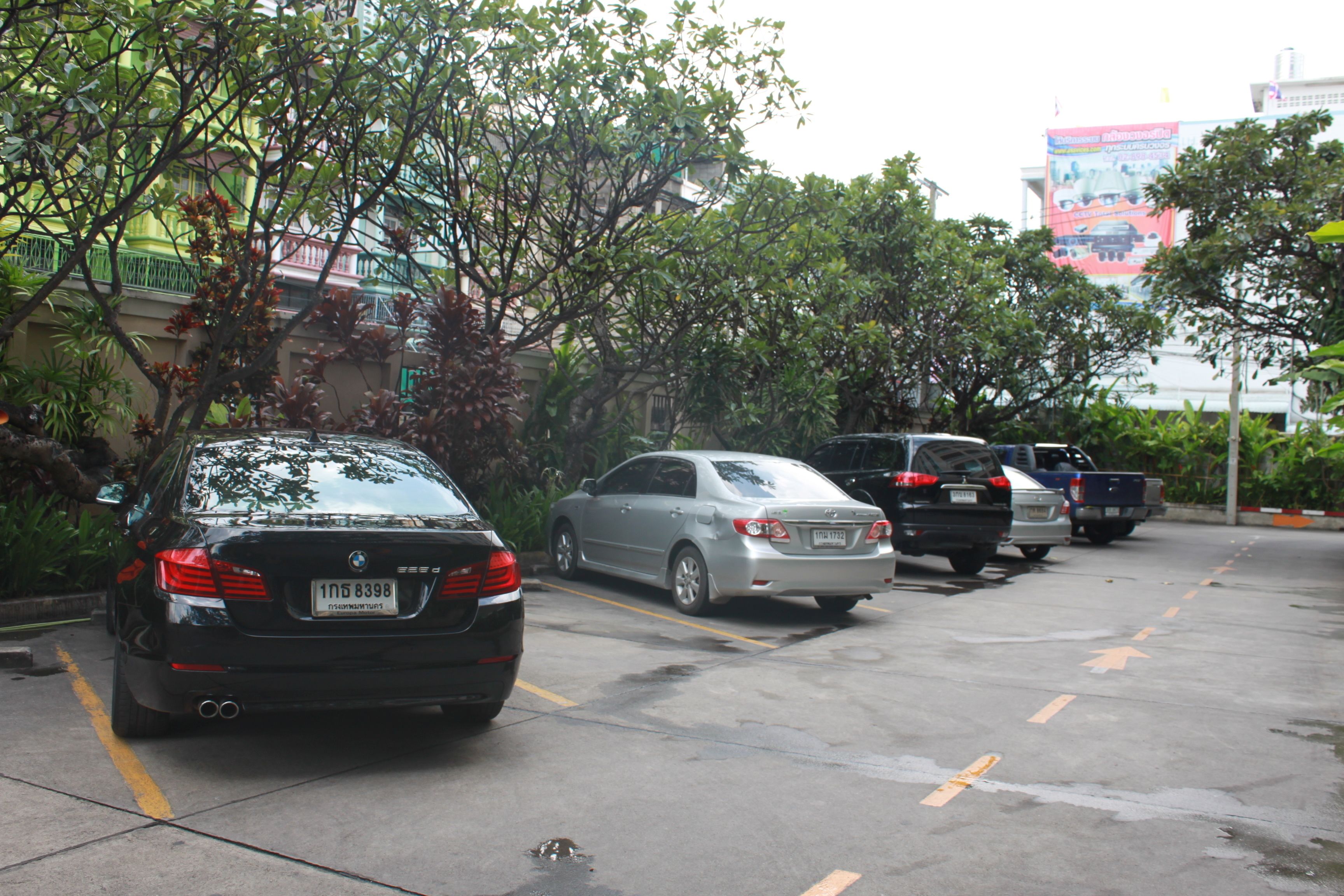 Un estacionamiento con varios autos estacionados, árboles y un edificio con un cartel publicitario al fondo.