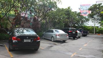Un estacionamiento con varios autos estacionados, árboles y un edificio con un cartel publicitario al fondo.