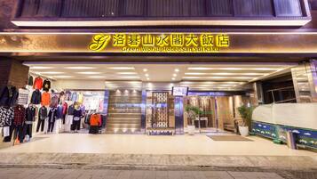 The exterior of the Green World Hotel-San Sui Ku with a prominent entrance, a display of clothing on the left, and a bench outside.