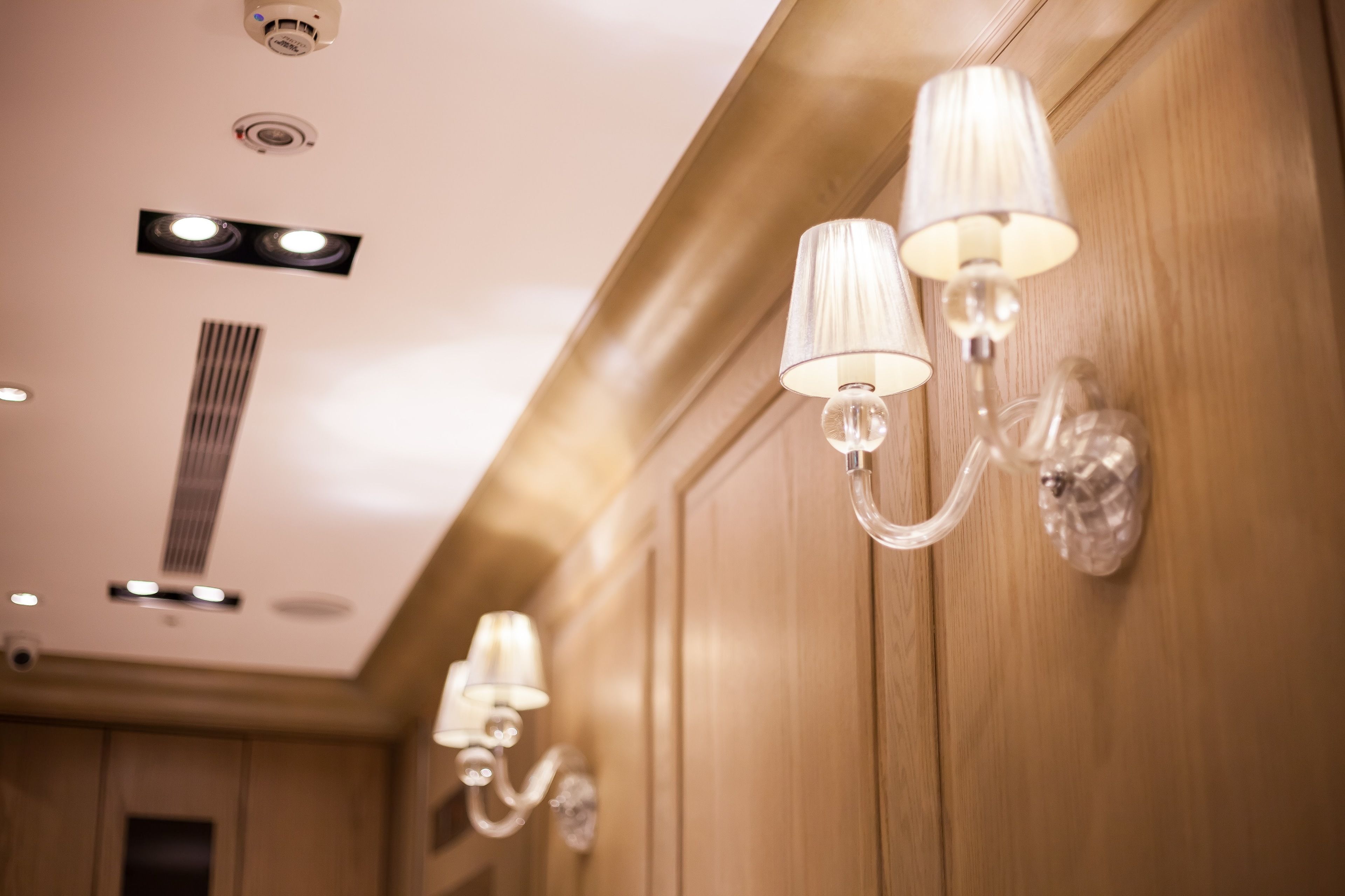 A hallway with wall-mounted sconces, a vent, and recessed ceiling lights.