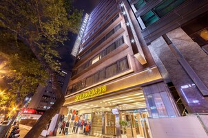 Een hotelingang met een bord in een vreemde taal, een winkel met kleding en een boom op de voorgrond.