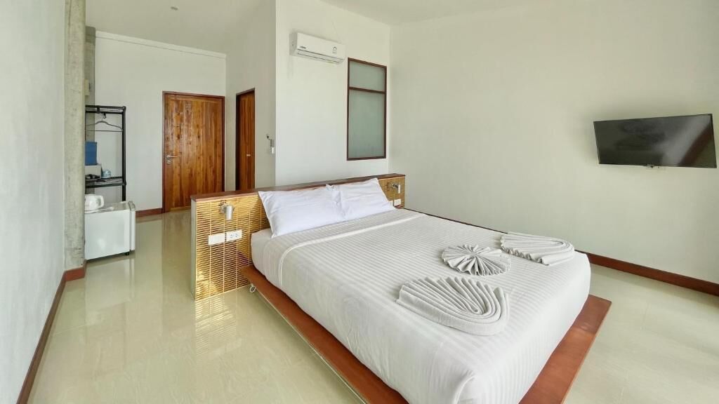 Quarto de hotel com uma cama grande, televisão na parede e porta de madeira.
