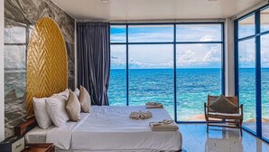 A bedroom with a large bed, a view of the ocean, and a chair by the window. - P.D. Beach Resort (Koh Tao)