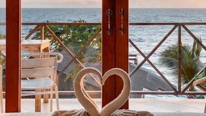 A room with a view of the sea at sunset, featuring a bed with two swan-shaped pillows and a wooden door. - P.D. Beach Resort (Koh Tao)