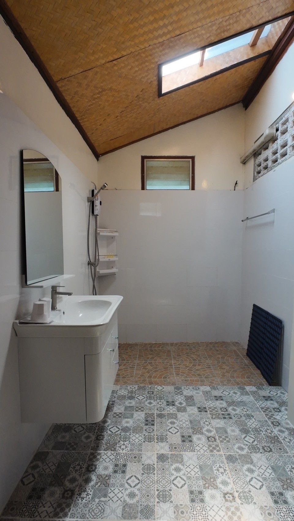 A bathroom with a sink, mirror, shower, and patterned floor tiles.