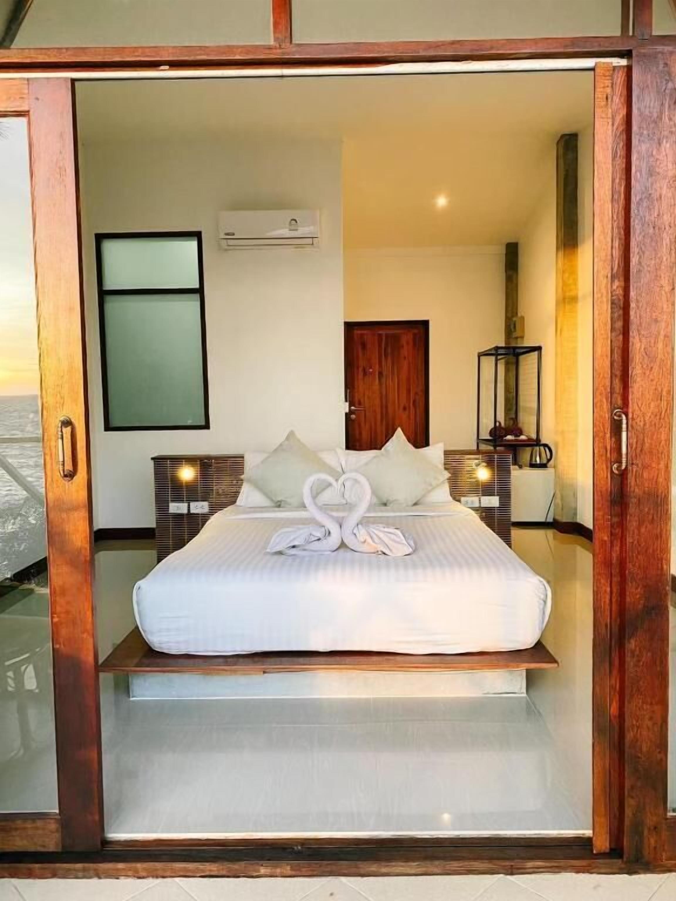A bedroom with a bed, a wooden door, a wall-mounted air conditioner, and a bedside table with a lamp.