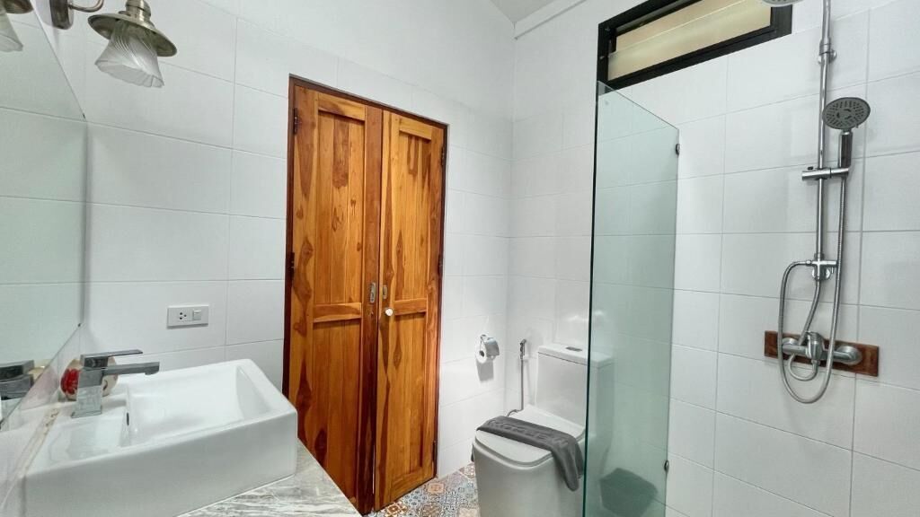 Un bagno con porta in legno, lavandino bianco, WC e cabina doccia in vetro.