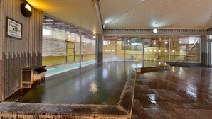 A traditional Japanese onsen with a wooden interior, a stone bath, and a view of the outside. - Hotel Marusansou (Chikuma)