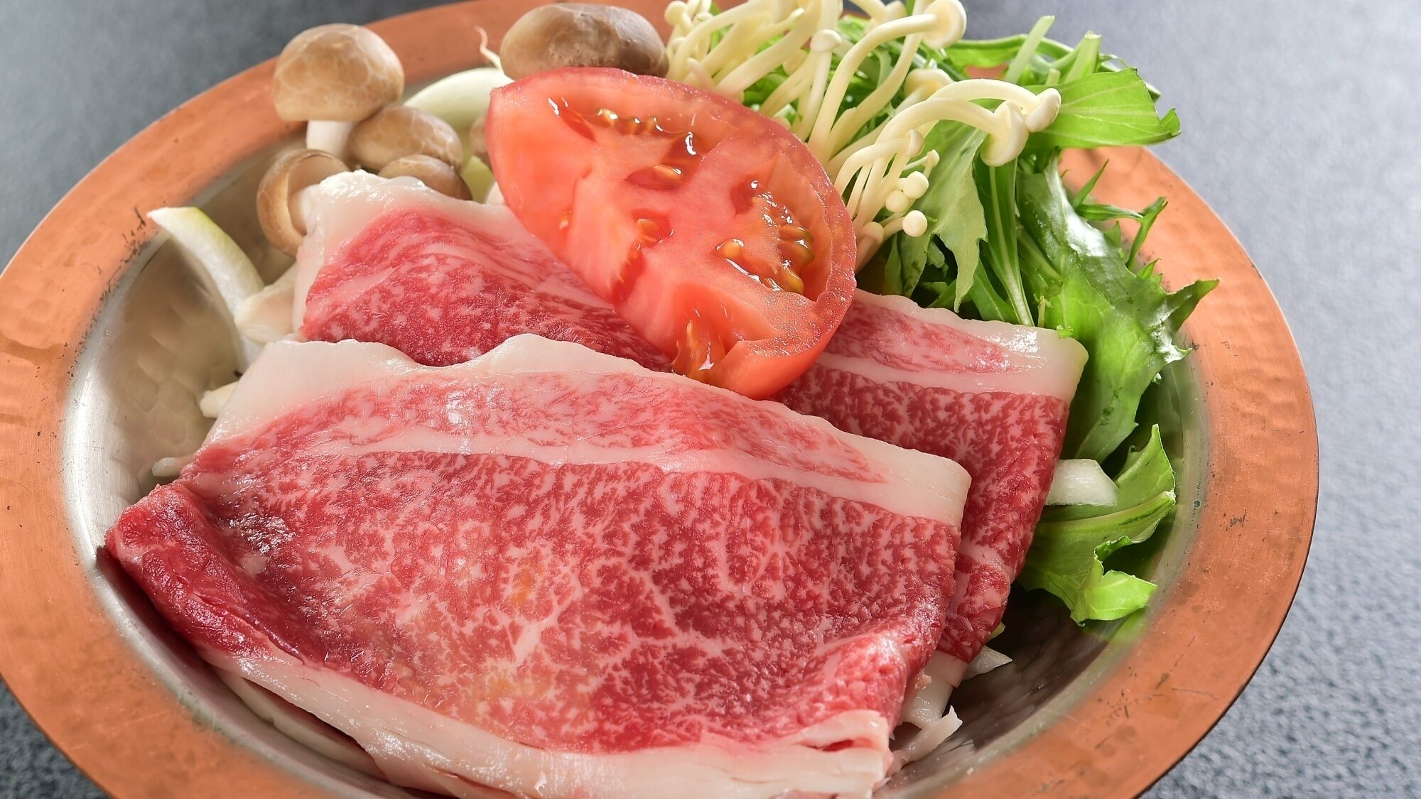 A plate with sliced meat, a tomato slice, mushrooms, and greens.